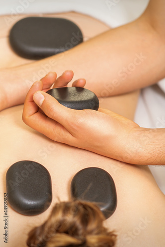 Hot stone massage on the female back with hands of masseur holding black massage stones in spa salon