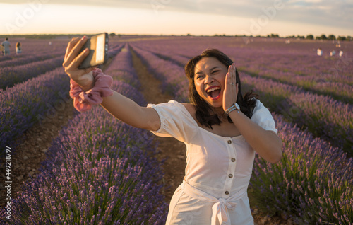 Fototapeta Naklejka Na Ścianę i Meble -  outdoors romantic portrait of young happy and attractive woman in white summer dress taking selfie with mobile phone at beautiful lavender flowers field in holiday concept