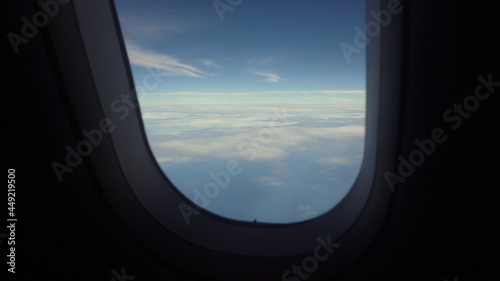 View from the porthole of an airplane on a blue sky and clouds. Airplane wing through the porthole. Looking through window aircraft during flight