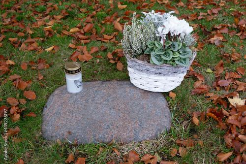 Steinplatte eines Rasengrabes mit Kerze und Blumenkorb im Herbst photo