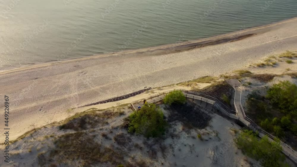 Sand beach next to green forest and blue ocean with people is filmed from above. Aerial drone footage of Curonian spit and Baltic sea in Kaliningrad. Tourist walk on wooden paths and observation deck. Sand beach next to green forest and blue ocean with people is filmed from above. Aerial drone footage of Curonian spit and Baltic sea in Kaliningrad. Tourist walk on wooden paths and observation deck.