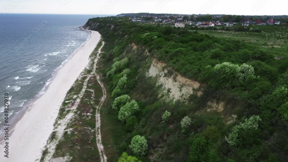 Aerial landscape of the long green cliff with town on it and rippled ocean. Drone footage of the Curonian spit and Baltic sea at cloudy summer day. There is a city on the mountain. Living on shoreline Aerial landscape of the long green cliff with town on it and rippled ocean. Drone footage of the Curonian spit and Baltic sea at cloudy summer day. There is a city on the mountain. Living on shoreline