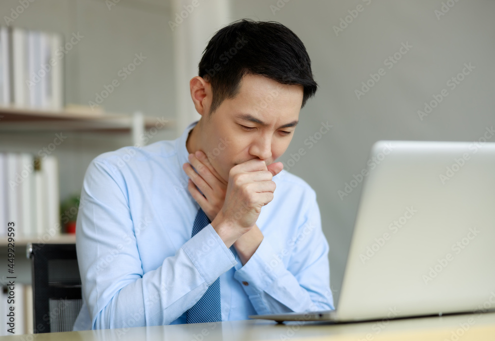 businessman working with laptop at desk in the office, hand at his neck, feeling unwell, have a sore throat,