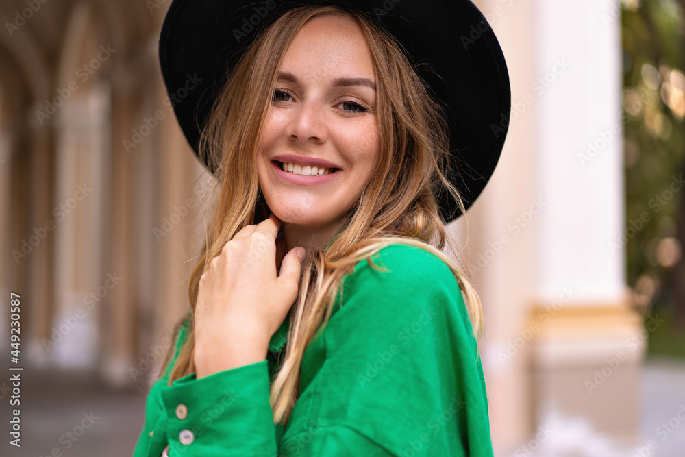 Sensual close up portrait of stylish blonde woman with curly hairs natural make up and pretty face, wearing black hat looking on camera , posing on the street, summer time.
