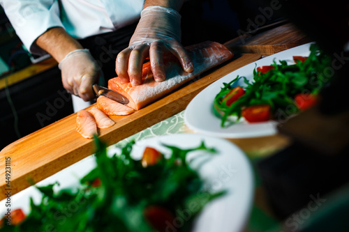 chef cuts frozen salmon fillet on dark background