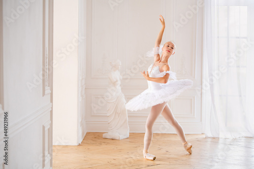 young slender ballerina in a white tutu standing on pointe at ballet bar in a beautiful white hall in front of a mirror.