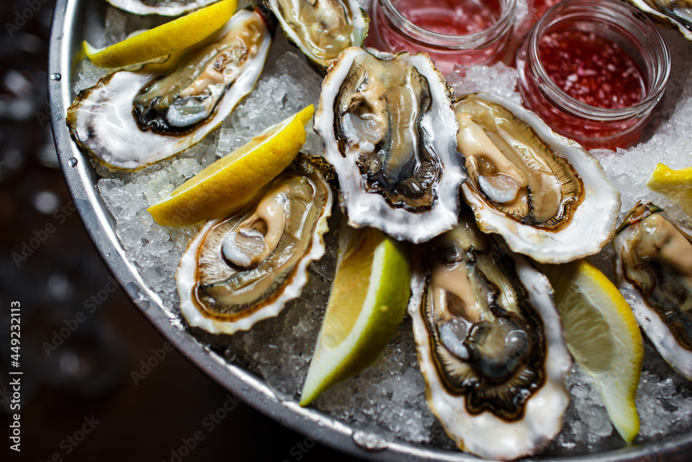 open oysters with lemon and sauce on a tray with ice on a dark background close-up