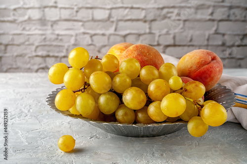 Ripe grapes and peaches in a metal wooden bowl on a gray table.