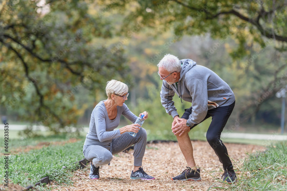 Senior couple jogging in the park taking a break. Man is having a knee injury Senior couple jogging in the park taking a break. Man is having a knee injury