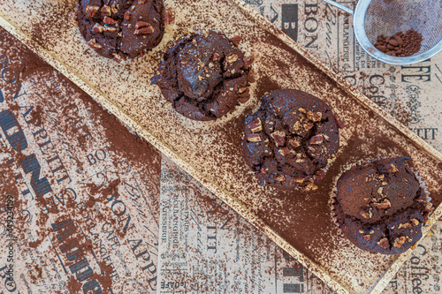 Healthy gluten free chocolate muffins with pecans on a wooden serving board. Homemade, freshly baked delicious cupcakes with a crispy top and cocoa powder. Nutrition concept, decorative background  