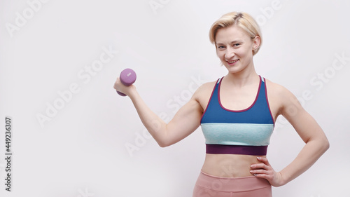Strong girl holding a dumbbell and dressed in activewear. Sporty girl posing for the camera. Concept of losing weight. Isolated over white background. Healthy lifestyle and good body condition.
