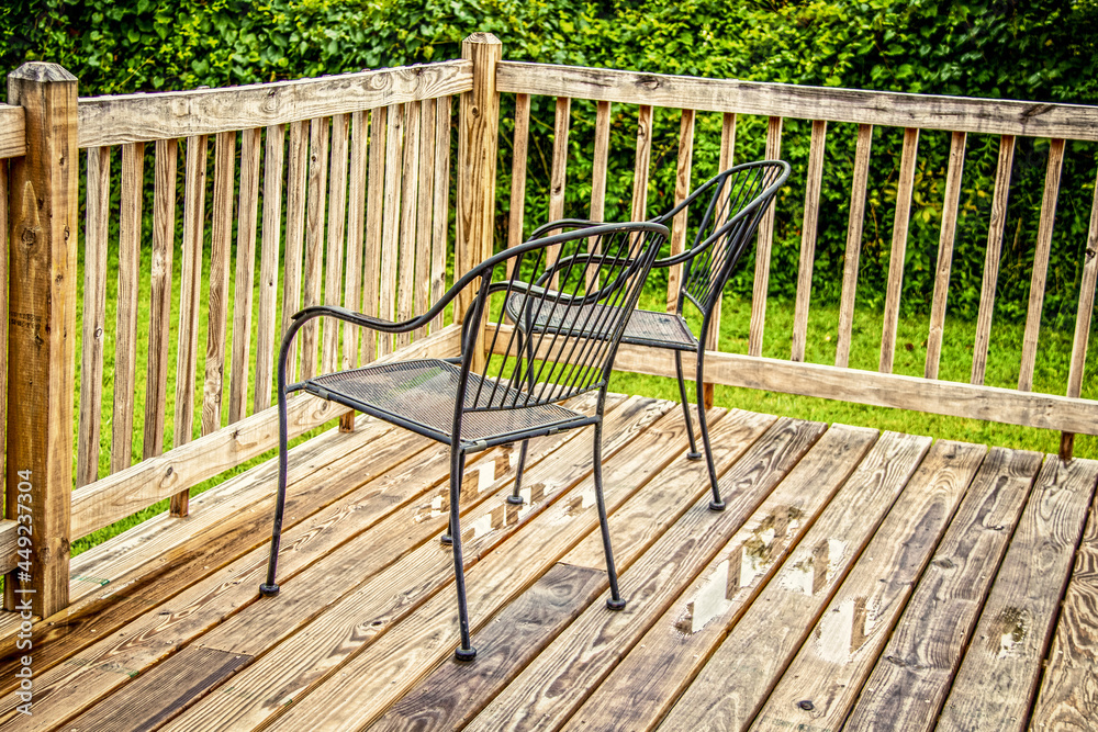 Two black metal lawn chairs sitting by rail on wooden deck after the rain with lush greenery in background. Two black metal lawn chairs sitting by rail on wooden deck after the rain with lush greenery in background.