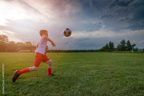 Boy playing with football ball on playing field. Child playing football. White - red football kit.