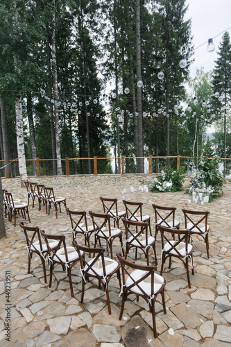 brown wooden chairs with cross-backs. Wedding decoration in nature, against the backdrop of the river and pine trees. natural wedding decor in a rustic style. holiday concept. © Anna