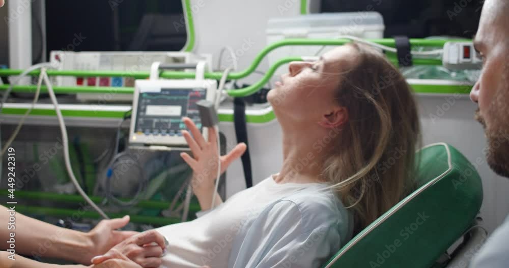 Tired Caucasian young woman pushing and breathing when giving birth to child in ambulance. Medic and husband supporting. Female in labor on way to hospital.