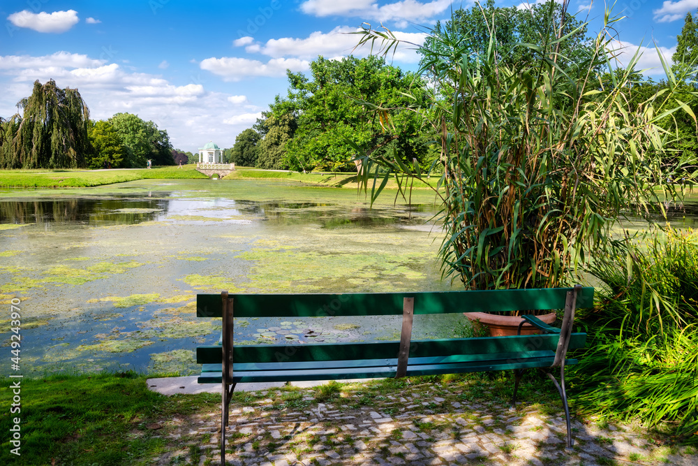 Obraz premium Idyllic place with bench to rest in the park Karlsaue with beautiful view to the swan island, Kassel, Germany