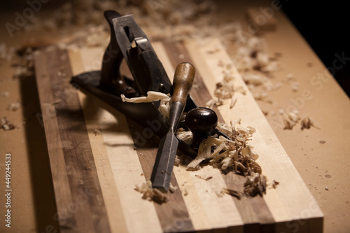 Antique hand planer and chisel on top of a butcher block surrounded by wood shavings.