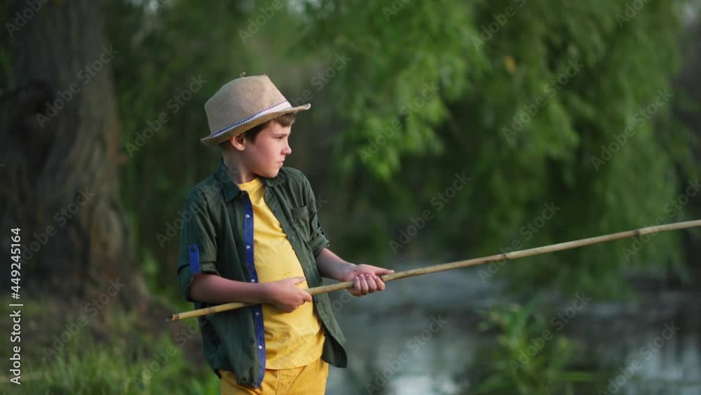 summer vacation, handsome male child in straw hat with fishing rod in his hands is fishing in river while relaxing in countryside summer vacation, handsome male child in straw hat with fishing rod in his hands is fishing in river while relaxing in countryside