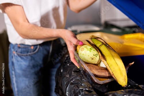 Close-up photo of Woman throwing fruits in the trash sorting waste, Zero Waste Concept. cropped eco-friendly woman throwing fruit into blue recycle bin indoors, sorting garbage to trash container