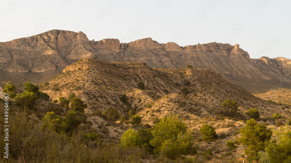 Desert and arid landscape with large mountains of orange earth in the province of Alicante (Spain). Dry mountains and plants due to drought.
