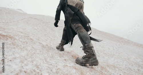 Close-up following shot of female legs stepping. Wide angle post apocalyptic female in futuristic grunge black clothes feet climbing hill in dead desert. Cyberpunk future warrior survivor after war photo