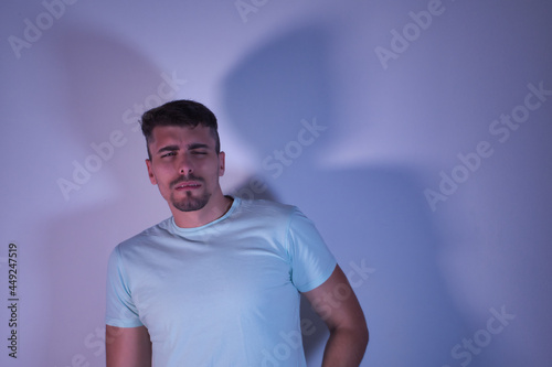 Young Hispanic male with one eye open and one eye closed with a distrustful gesture on white background.