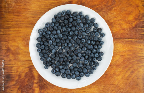 Ripe blueberries in a white plate on a wooden table.