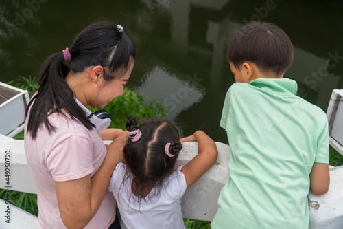 Young Asian mother walking by summer river with her kids. Woman shows nature landscape to her kid. Family spends time together