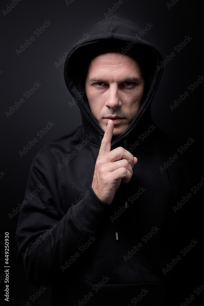 Maniac man ask to keep silence gesture, holding finger near mouth, looking at camera confidently, want to commit a crime, kidnap child. Caucasian guy in black wear isolated on black studio background Maniac man ask to keep silence gesture, holding finger near mouth, looking at camera confidently, want to commit a crime, kidnap child. Caucasian guy in black wear isolated on black studio background