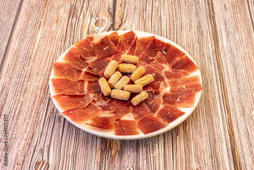 One of the most popular Spanish tapas of all time. A good plate of Iberian ham well cut by a specialist in the matter of cutting and with some bread rustic picos in the center. photo