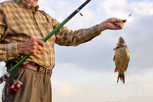 Hobby sport activity. Fish farming pisciculture raising fish commercially. Pensioner leisure. Fish on hook. unrecognizable fisherman catch fish. Cropped male alone stand near river. close-up hands