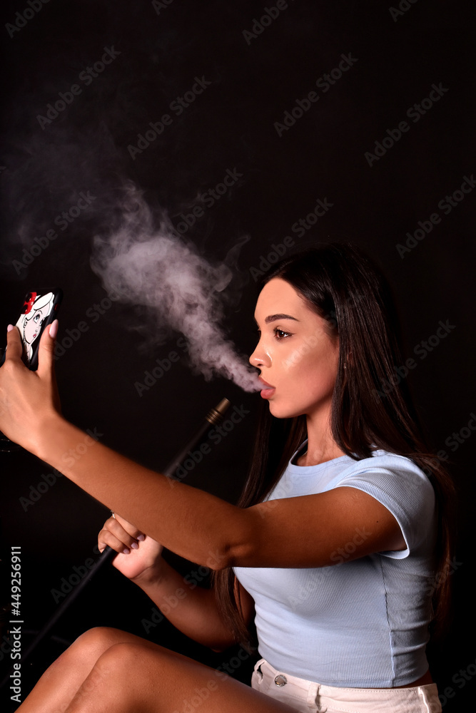 Young girl smokes a hookah and takes a selfie on a mobile phone. Fashion