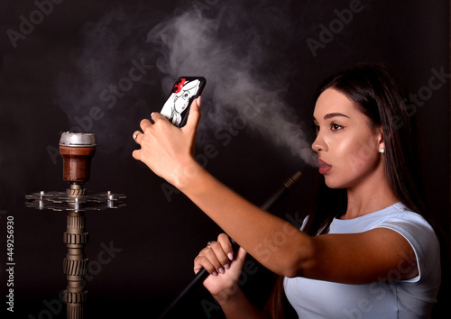 Young girl smokes a hookah and takes a selfie on a mobile phone. Fashion