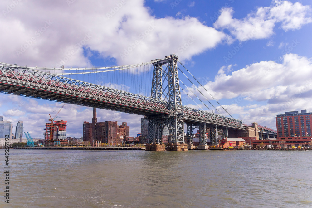 A picture of Williamsburg Bridge in New York City, USA. In the picture one can see the East River, Brooklyn and Domino Sugar Refinery and park