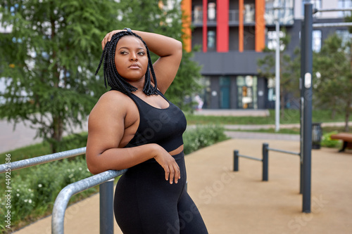 Side View Portrait Of Young Fat Overweight Woman In Sportive Outfit Posing Outdoors After Sport Workout, Have Rest, Taking A Break During Exercises, Looking At Side Confidently. Copy Space, Sport