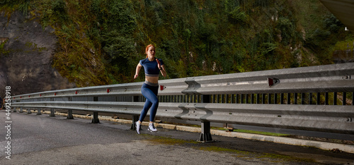 Female athlete running on modern bridge near forest. woman fitness jogging workout wellness concept. Side view on confident lady with ponytail running fast, in nature. copy space. people lifestyle © Roman