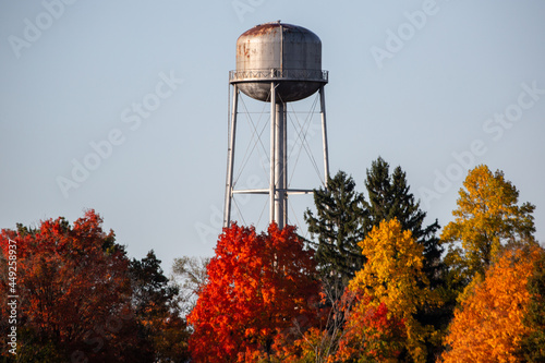 A vintage steel small town water tower standing in morning light and blue skies surrounded by fall color autumn trees_06
