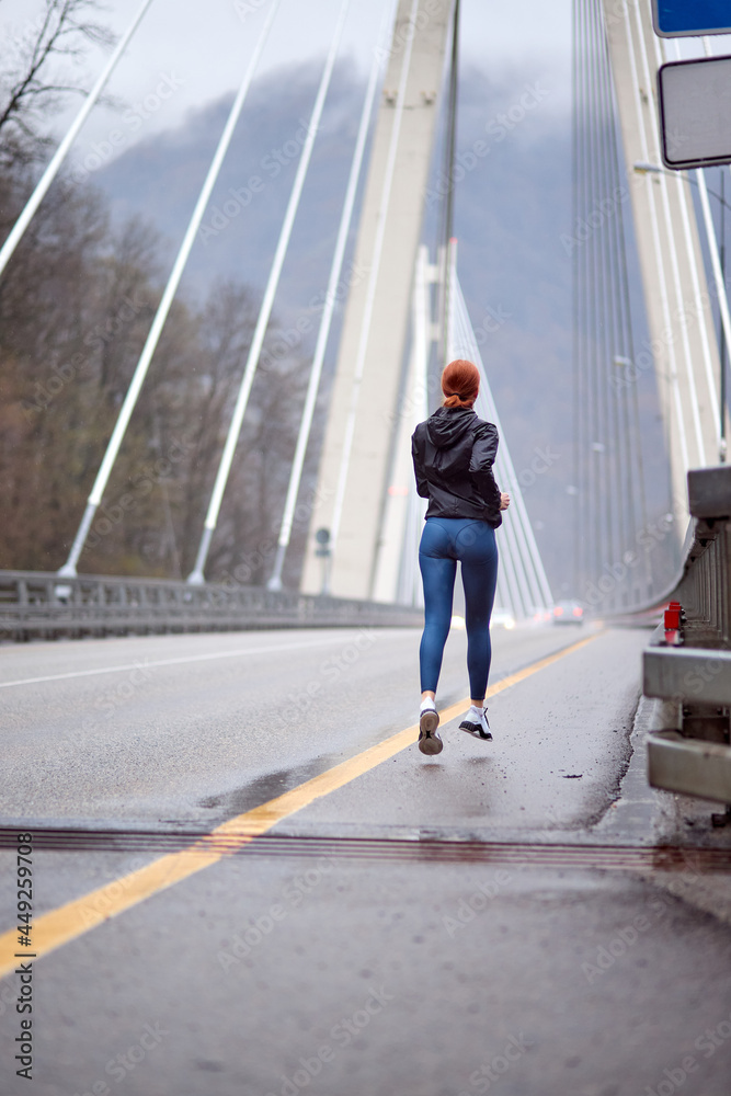 Rear view runner outdoors running on the bridge, portrait of confident female athlete in sportive outfit jogging in the morning, sport activity in nature, foggy day. people lifestyle, sport concept