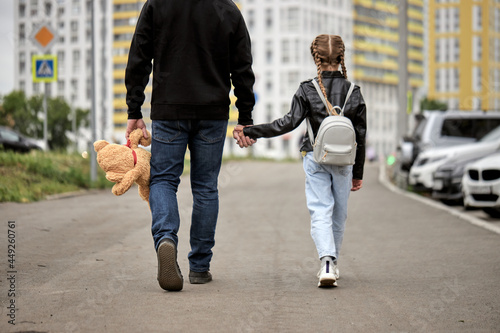 Pedophile man holds the hand of teenage girl in street. The concept of kidnapping and child trafficking. Rear view on pedophile with toy and caucasian child girl walking along the street. Crime photo
