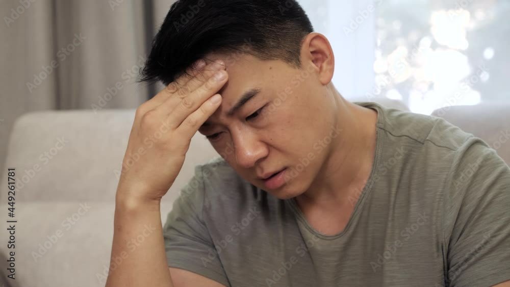 Exhausted frustrated young chinese man massaging nose bridge temples. Stressed unhealthy millennial mixed race freelancer feeling tired suffering from migraine, panic attack, high blood pressure. Exhausted frustrated young chinese man massaging nose bridge temples. Stressed unhealthy millennial mixed race freelancer feeling tired suffering from migraine, panic attack, high blood pressure.