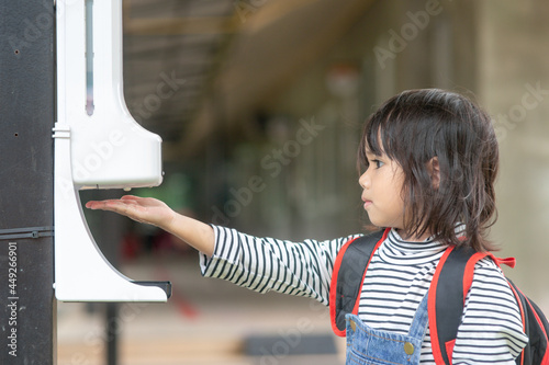 Child girls kid using automatic alcohol gel dispenser spraying on hands sanitizer machine antiseptic disinfectant, new normal life after Coronavirus COVID-19 pandemia.