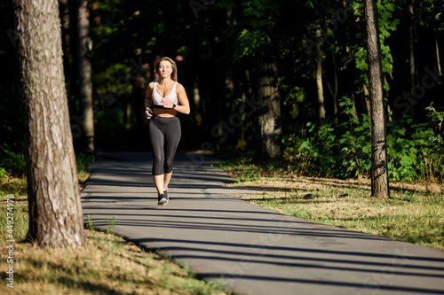 Evening jogging in park, young woman runs along asphalt path.