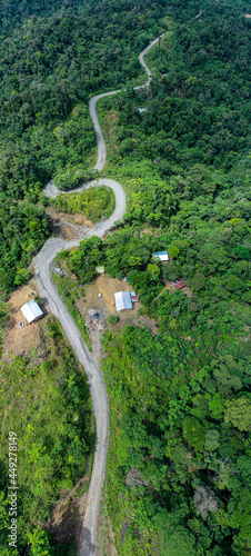 Aerial panorama of a dirt road winding through the hills in a forest with a few houses alongside