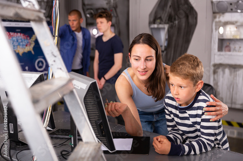 Young mother with her preteen son spending funny time in quest room decorated as lost underground shelter, trying to solve puzzle on computer monitor