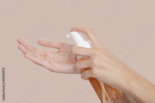 pours body and face lotion from a bottle into her hand. beige background