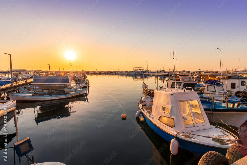 tranquil sunrise in fishing docks at a small port with calm sea and golden sun , old sailing boats moored around marina