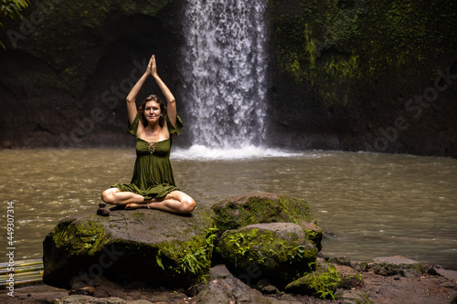 Namaste mudra. Lotus pose. Caucasian woman sitting on the stone  meditating  practicing yoga  pranayama at waterfall. Hands raised up in namaste mudra. Yoga retreat. Tibumana waterfall  Bali