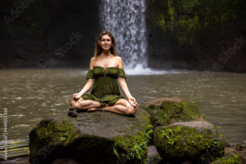 Yoga lotus pose. Gyan mudra. Young Caucasian woman sitting on the stone  meditating  practicing yoga  pranayama at waterfall. Hands in gyan mudra. Yoga retreat. Tibumana waterfall  Bali