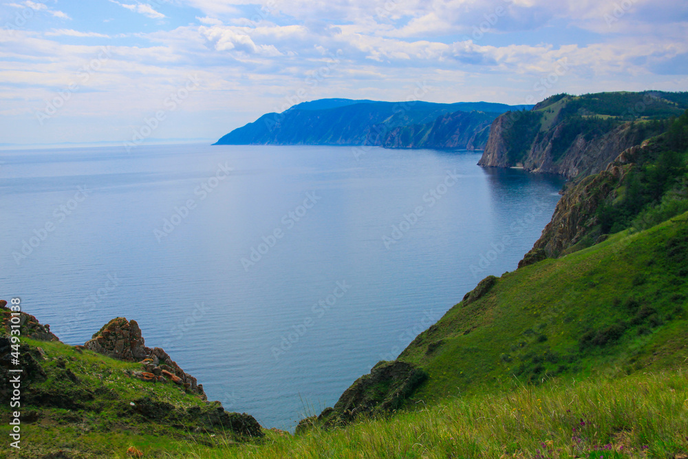 A beautiful summer landscape. A blue bay reflects a bright sky. A coastline of the Lake Baikal. Wonderful views of the Olkhon island.  A green meadow on the shore.