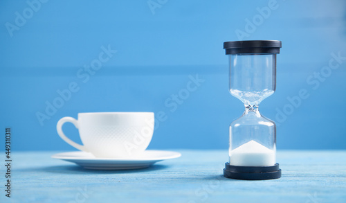 Hourglass and coffee cup on the blue background.